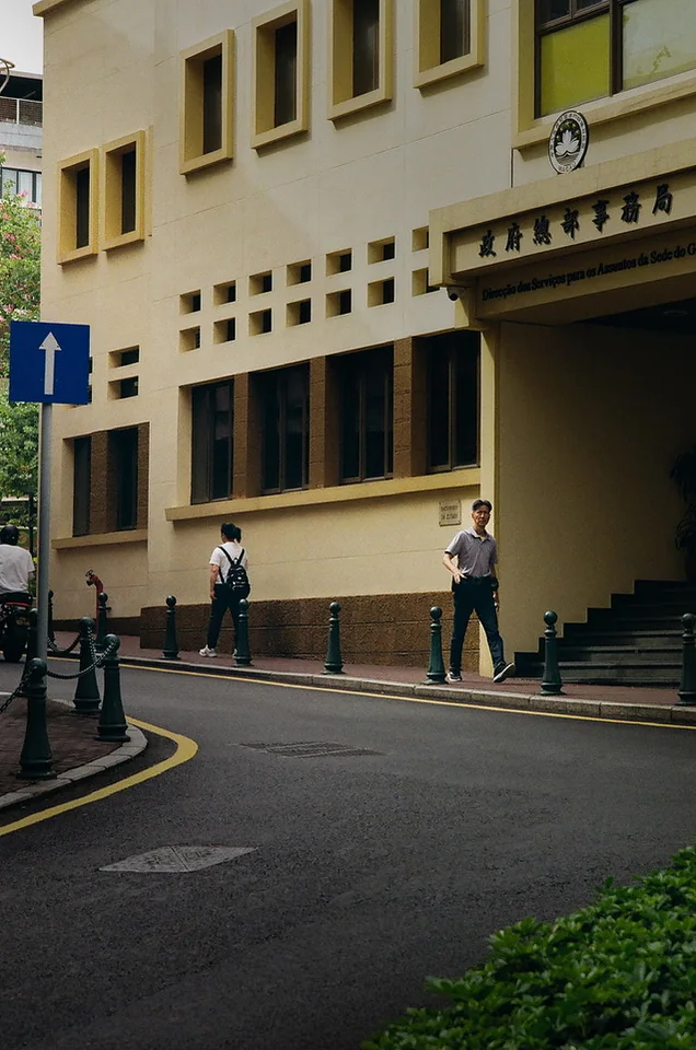 Pedestrians passing a pale building along a curved street