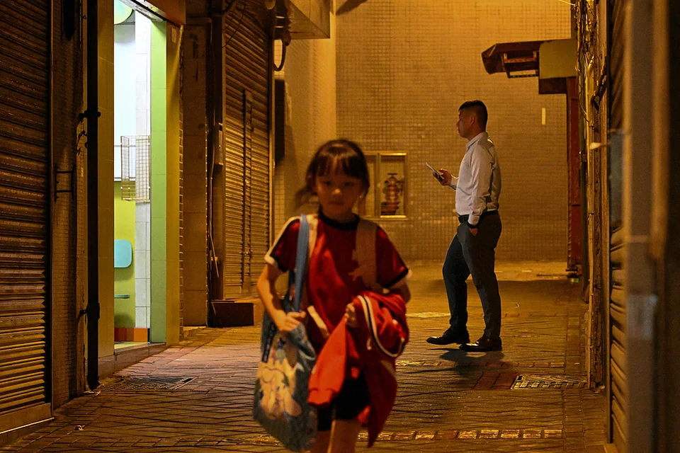 A child passing through a warmly lit alley, with a man standing behind her