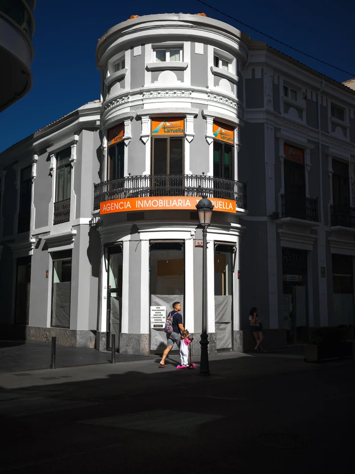 An adult and child passing a white corner building