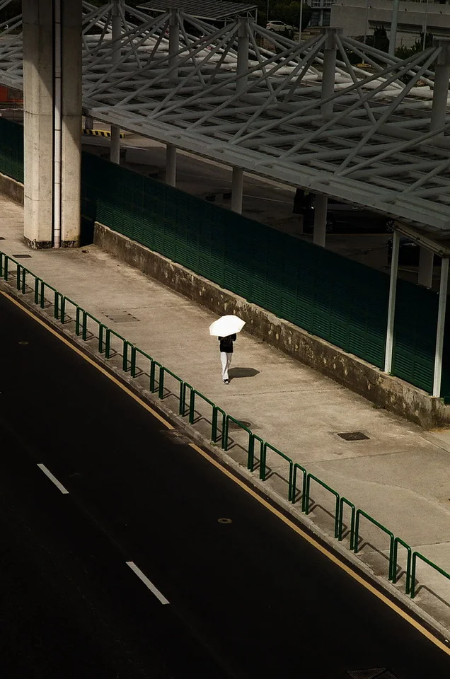 A person with a white umbrella walking through sunlight beside green railings