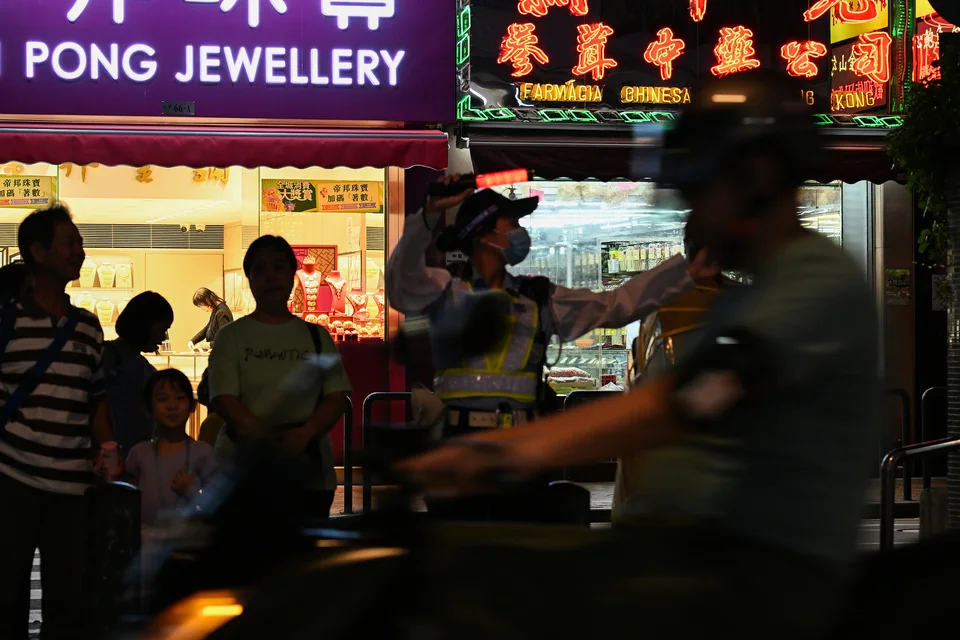 People waiting by neon-lit shops while a motorcycle passes